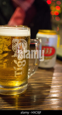 Primo piano di una tazza di Thai birra Tiger con lattina di birra in background in Bangkok Foto Stock