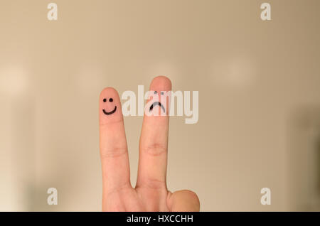 Due disegnati a mano emoticon si affaccia su una delle persone dita , un felice e sorridente e l'altro infelice, triste o depressa isolata su uno sfondo neutro wi Foto Stock