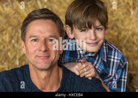 Felice padre e figlio di uomo e ragazzo che sorride seduto sul fieno o balle di paglia Foto Stock