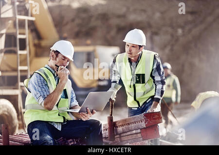 Caposquadra e lavoratore edile utilizzando il portatile in sito in costruzione Foto Stock