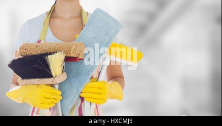 Digital composito della donna in grembiule con spazzole contro sfocate camera grigia Foto Stock