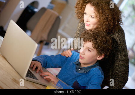 Ritratto di una madre aiutare suo figlio utilizzano il computer a casa Foto Stock