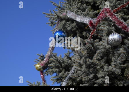 Decorazioni Anno nuovo albero. Tinsel e giocattoli, le sfere e le altre decorazioni di Natale sulla struttura ad albero di Natale in piedi in aria aperta. Foto Stock