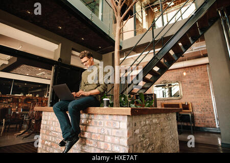 Giovane uomo seduto in ufficio bar che lavora sul computer portatile. Creativi esecutivi utilizzando il computer portatile durante la pausa caffè. Foto Stock