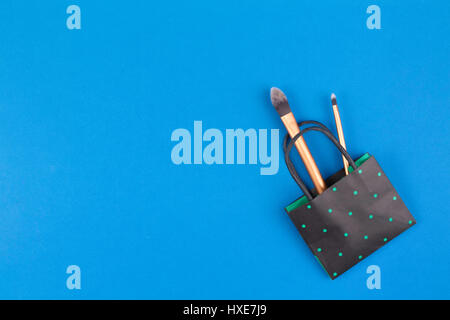 Make up pennelli con nero polka dot paper shopping bag su sfondo blu. Vista dall'alto. Lay piatto. Foto Stock