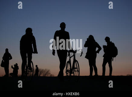 Sagome di persone con le loro biciclette al tramonto su Parliament Hill, Hampstead Heath, a nord di Londra. Foto Stock