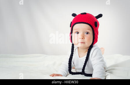 Carino il bambino giacente sul letto su coltre bianca in ladybug hat Foto Stock