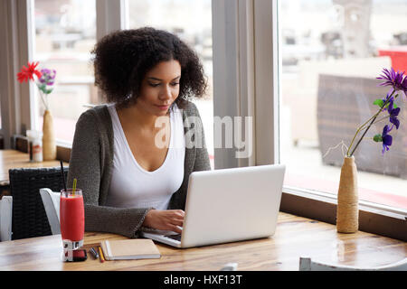 Ritratto di un americano africano giovane donna seduta al cafe con laptop scrivendo il suo blog Foto Stock