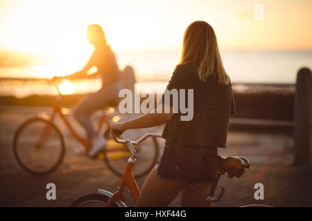 Donna in piedi con la bicicletta su strada durante il tramonto Foto Stock