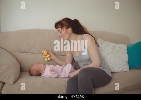 Amorevole Madre mostra giocattolo per bambino sul divano di casa Foto Stock