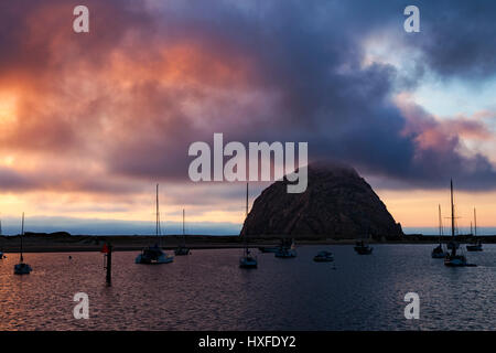 La nebbia si siede al picco di Morro Rock come il sole tramonta dietro il Morro Bay Harbour lungo la costa della California. Foto Stock