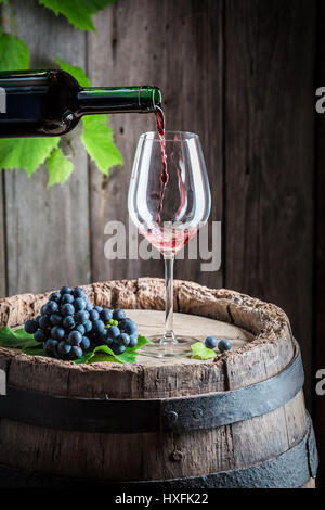 Versando il vino rosso su vetro sulla canna con uve Foto Stock