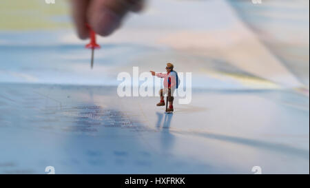 Lato immissione di un pin di colore rosso con figurine in miniatura di lonely giovani viaggiatori con zaino camminando sulla mappa grande Foto Stock