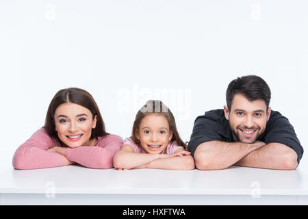 La famiglia felice con un bambino appoggiato sul tavolo bianco e sorridente Foto Stock