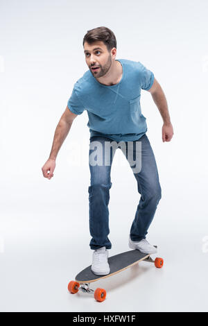 Uomo che cerca di cavalcare skateboard su bianco Foto Stock