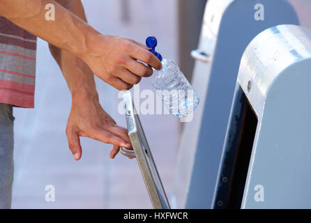 Stretta di mano maschio mettendo la bottiglia di plastica nel contenitore di riciclaggio Foto Stock