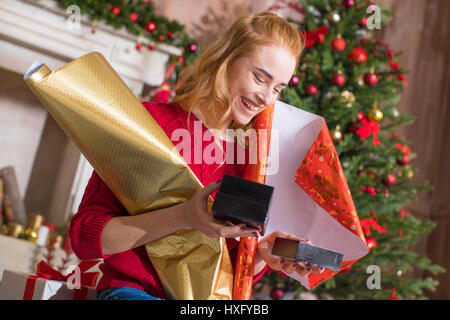 Felice ragazza bionda holding di rotoli di carta di avvolgimento e guardando a confezioni regalo Foto Stock