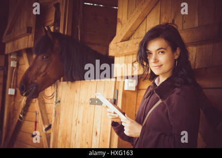 Lavoro femminile sulla tavoletta digitale accanto al cavallo stabile Foto Stock