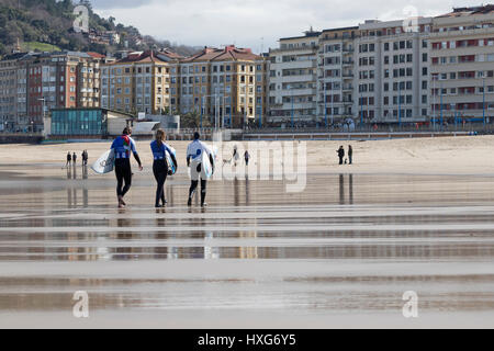 Tre i surfisti a piedi dall'acqua alla spiaggia Zurriola (San Sebastian, Paese Basco) 2017. Foto Stock