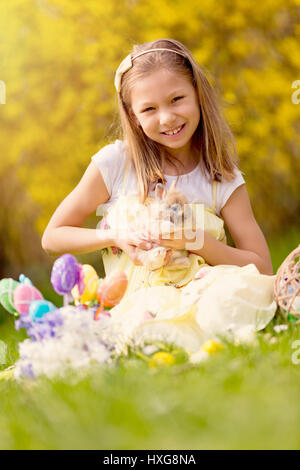 Bella sorridente bambina holding carino bunny e seduto sul prato di vacanze di primavera. Foto Stock