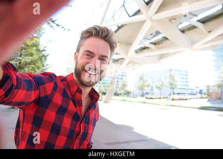 Uomo sorridente tenendo selfie al di fuori della città Foto Stock