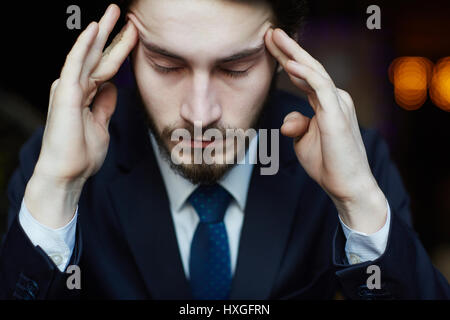 Testa e spalle ritratto di bello uomo barbuto indossando eleganti business suit, templi di sfregamento e chiudendo gli occhi affetti da mal di testa e stress Foto Stock