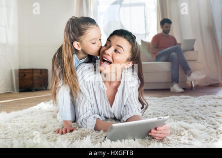 Madre e figlia divertirsi mentre giaceva sul tappeto e con tavoletta digitale Foto Stock