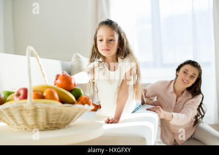 Ritratto di ragazza picking tangerine dal cesto con la madre dietro Foto Stock
