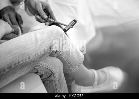 Vista parziale del medico esaminando ragazza paziente con martello di riflesso, foto in bianco e nero Foto Stock