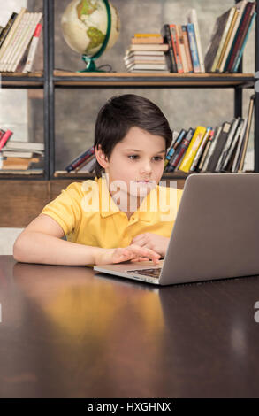 Concentrato schoolboy seduta a tavola e Utilizzo di computer portatile Foto Stock