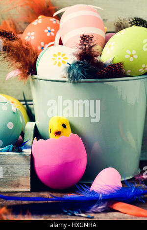 Primo piano di un giocattolo di chick emergente da un uovo rosa, una pila di differenti decorate le uova di pasqua e piume di diversi colori Foto Stock