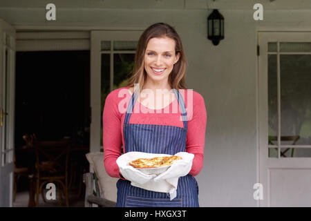 Ritratto di una donna sorridente tenendo la torta in una teglia Foto Stock