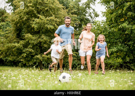 La famiglia che giocano a calcio in estate con i loro figli Foto Stock