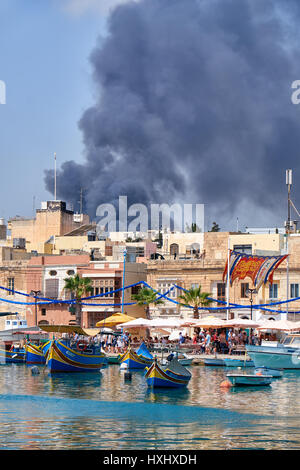 MARSAXLOKK, Malta - 1 agosto 2015: la vista del fumo dal fuoco su di Marsaxlokk villaggio di pescatori, Malta Foto Stock