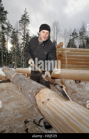 Regione di Leningrado, Russia - 2 Febbraio 2010: Il processo di distacco e di scortecciatura del legno, lavoratore pelate a mano i registri per log cabin costruzione. Foto Stock