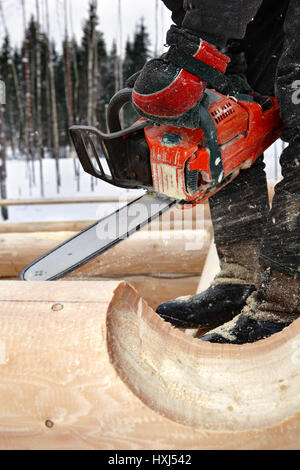 Regione di Leningrado, Russia - 2 Febbraio 2010: costruzione di log house close-up di mani lavorando con una motosega, lavorazione del legno. Foto Stock