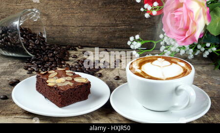 Cappuccino caffè e dolce brownie al cioccolato torta. Una tazza di latte, cappuccino o un espresso con il latte su un tavolo in legno scuro con la tostatura i chicchi di caffè. Foto Stock