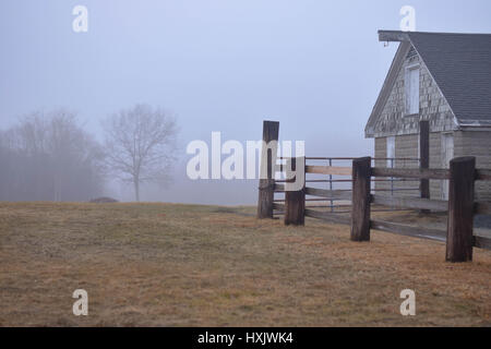 Fienile e una recinzione con alberi nella nebbia Foto Stock