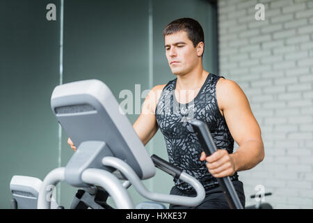 Uomo muscolare mediante macchina ellittica durante gli allenamenti in palestra Foto Stock