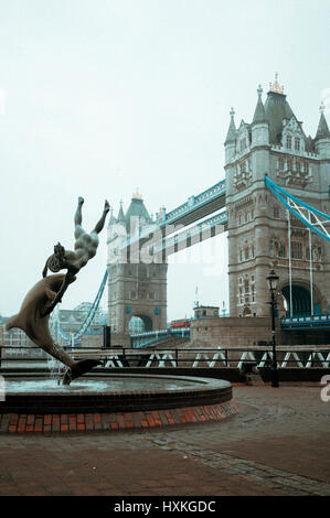 L'immagine verticale di Tower Bridge in una nebbia meteo con David Wynne della ragazza con un delfino statua in primo piano, Londra, Regno Unito. Foto Stock