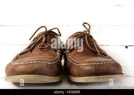 Coppia di usurati brown casual scarpe in pelle di fronte bianco sullo sfondo di legno Foto Stock