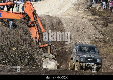 Un escavatore per tirare fuori le vetture stradali fuori della trincea fangosa. un veicolo fuoristrada è la guida a pieno regime da trench in salita in un fango. Foto Stock