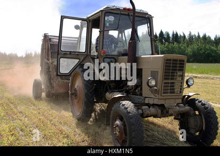 Lemozero, Olonets, Carelia, Russia - Luglio 26, 2006: Farm ruota del trattore con round fienagione rotopressa su la raccolta di fieno nel campo, russo farmland. Foto Stock