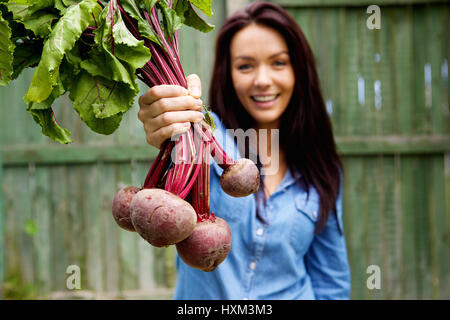 Close up ritratto di una donna sorridente che mostra un mazzetto di barbabietole Foto Stock