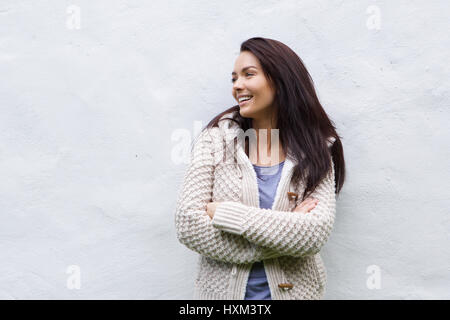 Ritratto di una donna sorridente in maglia di lana in piedi contro il muro bianco Foto Stock