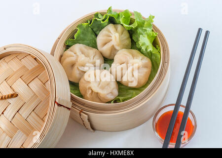 Carne di maiale al vapore panini Asian dim sum nel cestello di bambù, servire con bacchette e salsa su uno sfondo bianco, Chiusi Foto Stock