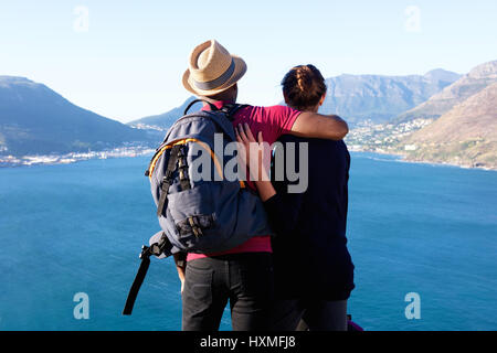 Vista posteriore del ritratto di amorevole coppia giovane seduto su una scogliera a guardare la bella vista Foto Stock