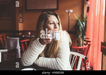Ritratto di giovane bellissima femmina a bere caffè e guardando con sorriso fuori del coffee shop finestra mentre godendo il suo tempo libero - break, happin Foto Stock