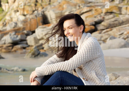 Ritratto di una donna sorridente seduti all'aperto in un maglione che guarda lontano Foto Stock