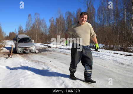 Nazia village, regione di Leningrado, Russia - 17 Marzo 2015: Veicolo bloccato sulla strada di ghiaccio in foresta, la ruota anteriore è caduto in un buco, il driver utilizza un verricello t Foto Stock